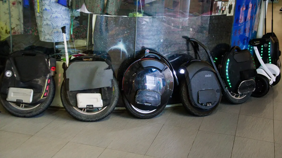A row of electric unicycles parked side by side against a wall